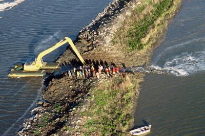 Dirt-mover tears open an Island Ponds levee as the crowd watches. Credit: Marc Bittner
