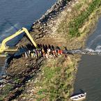 Dirt-mover tears open an Island Ponds levee as the crowd watches. Credit: Marc Bittner